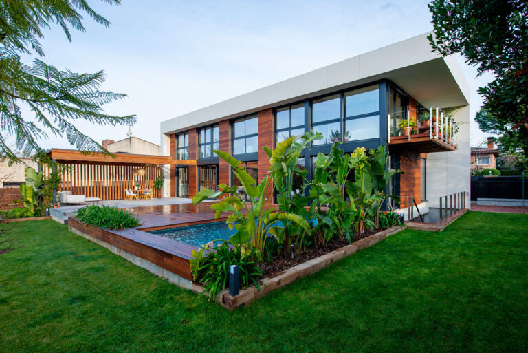 Vistes de la casa des de l'exterior. Es pot veure la piscina amb el terra de fusta, el porxo i dues façanes de la casa.